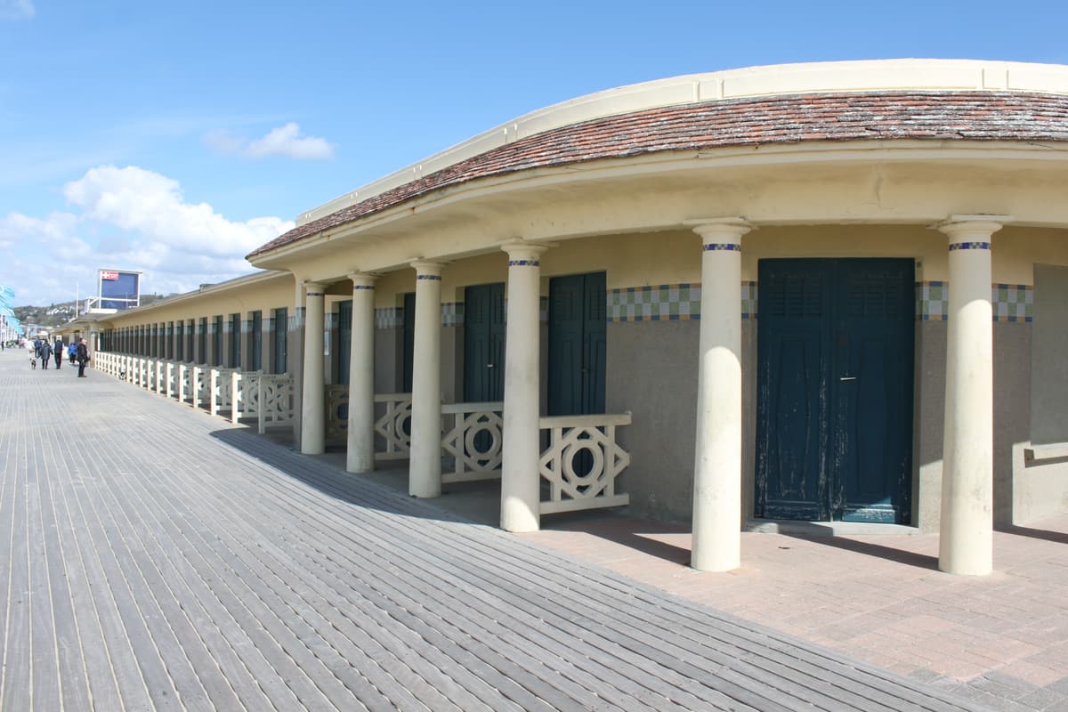 Galerie courbe à colonnes blanches et toit de tuiles, ornée d'une frise de carreaux bleus et verts, le long d'une promenade en planches.