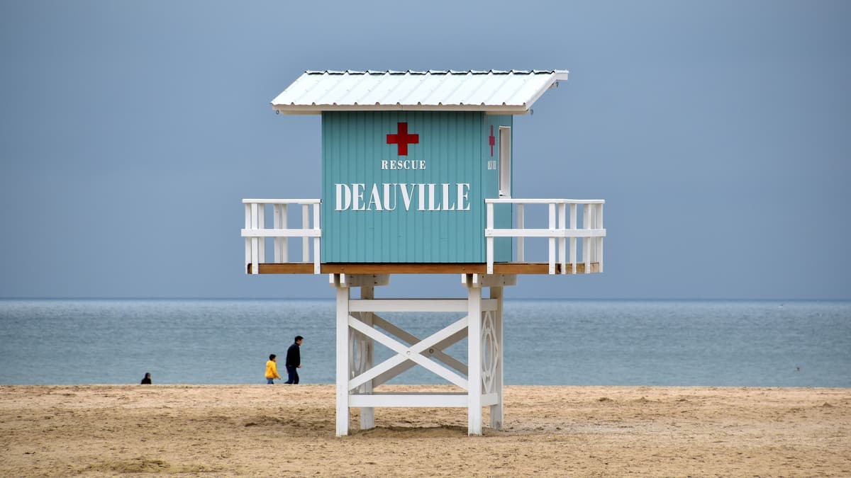 Poste de secours en bois bleu et blanc, monté sur pilotis, portant l'inscription « Deauville », sur le sable devant la mer.