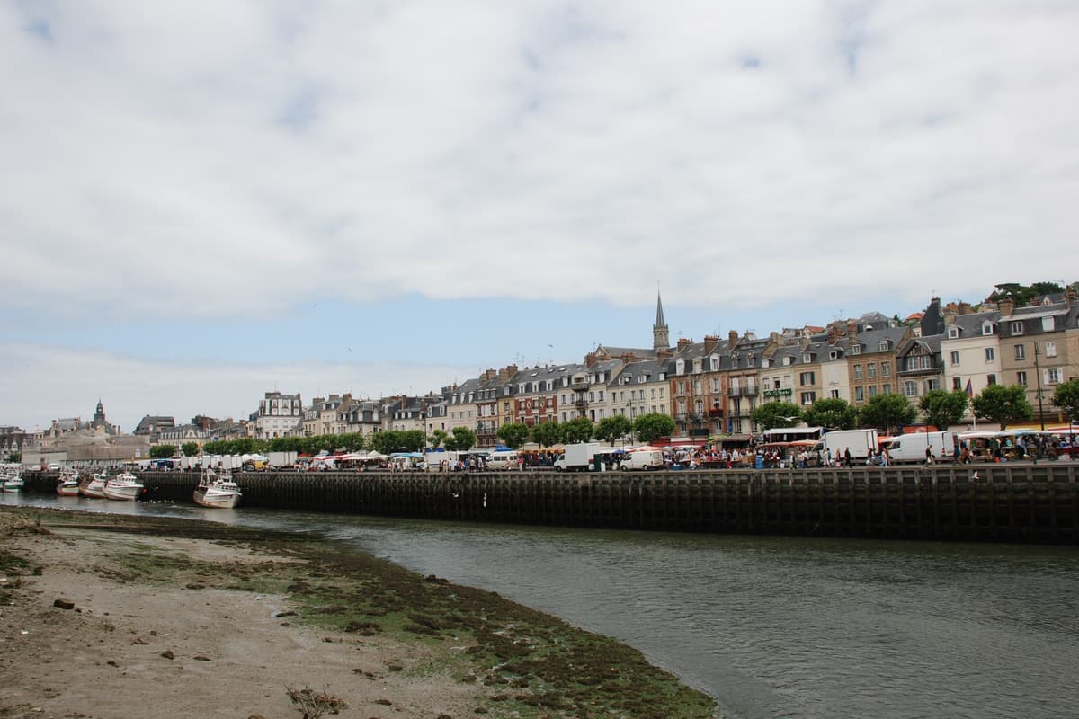 Rive vaseuse de la Touques à marée basse, un quai et, en face, les façades de Trouville-sur-Mer et un clocher.